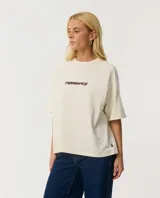 Remera Rip Curl de manga corta, color beige, con diseño boxy y estampado gráfico en la espalda de la competencia de surf Rip Curl Cup en Sunset Beach, Hawaii.