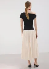 Vestido largo de diseño asimétrico con cuerpo negro entallado de cuello barco y manga corta, combinado con una falda larga evasé en color beige claro.
