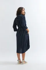 Vestido camisero midi de lino color azul marino con rayas verticales blancas, corte holgado, cuello camisero, mangas 3/4 con puños elásticos y lazo en la cintura.