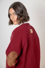 Saco de punto color beige, con cierre frontal de botones marrones y detalle de costuras decorativas oscuras en los hombros. Presenta un diseño clásico con cuello redondo.