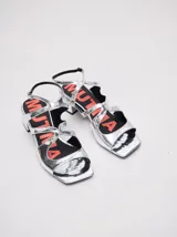 Sandalias de cuero con acabado de charol metalizado en color dorado, con tiras cruzadas en el empeine, taco cuadrado de 4,5 cm y correa ajustable en el tobillo.