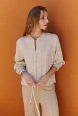 Bomber de tela liviana color beige con textura sutil, cierre frontal completo, mangas largas con puños elásticos y cordón ajustable en el ruedo.