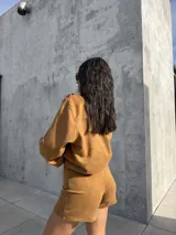 Campera de estilo bomber confeccionada en tejido tipo gamuza scuba, color marrón tostado. Presenta cierre frontal, cuello camisero, puños y ruedo elásticos, brindando un ajuste cómodo y versátil.