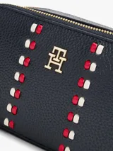 Cartera tipo bandolera Tommy Hilfiger de acabado granulado en color azul marino. Cuenta con dos compartimentos principales con cierre de cremallera, correa ajustable y detalles metálicos dorados. En el frente presenta el monograma TH metálico y una cinta decorativa vertical con los colores distintivos de la marca.