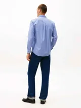 Camisa de hombre de manga larga, confeccionada en sarga de algodón mercerizado, con diseño de rayas verticales azules y blancas. Presenta cuello con botones, bolsillo de parche en el pecho con logo bordado de Tommy Hilfiger y puños redondeados con botón.