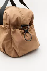 Bolso de nylon en color verde militar, con diseño deportivo, asas de mano resistentes, cierre superior y bolsillos laterales con frunce ajustable mediante cordón elástico.