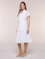 Vestido midi blanco de calce suelto y caída fluida, con escote en V, cuello a la base y apertura abotonada con detalle de puntilla. Cuenta con cintura elastizada con lazo para anudar a tono, mangas cortas con volados y falda con volantes escalonados.