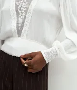 Blusa de viscosa color blanco con cuello alto, mangas largas con puños ajustados y detalles de encaje bordado en el frente y en los puños.