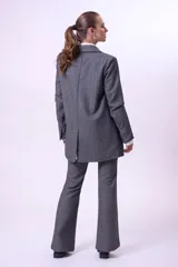 Blazer de corte sastrero en color gris con textura jaspeada. Presenta un diseño de doble botonadura, solapas clásicas y detalle de strass aplicado en una de las solapas. Cuenta con bolsillos laterales con solapa y mangas largas.