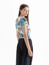 Top de punto color azul con estampado floral en tonos naranja, blanco y verde. Tiene escote redondo, mangas cortas y frunces laterales que estilizan la figura.