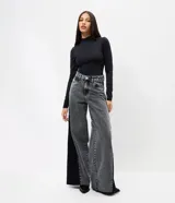 Pantalón wide leg de jeans color gris lavado, con diseño de tiro medio y cierre tradicional. Presenta un recorte lateral en color negro que recorre toda la pierna, aportando un contraste visual y estructura al modelo.