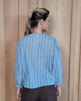 Camisa de manga larga con diseño de rayas verticales y bordados sutiles. Presenta cuello redondo, cierre frontal con botones y mangas abullonadas con volados en los hombros.