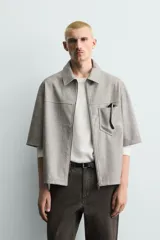 Sobrecamisa de manga corta efecto piel de corte relajado, color gris, con cuello solapa, bolsillo de parche en el pecho y cierre frontal con cremallera.