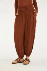 Pantalón de tiro alto y silueta amplia, estilo aladín, color marrón. Cuenta con cintura de pala ancha fruncida, bolsillos laterales y puños elásticos en los tobillos.