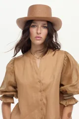 Blusa color tostado confeccionada en lino, con mangas abullonadas de ramie y detalles de bordado en punto smock en los puños.