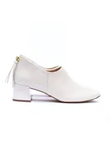 Zapato color blanco hueso con punta cuadrada, confeccionado en cuero nobuck y napa. Presenta un diseño con textura de piel de serpiente en la parte trasera, cierre de cremallera dorado en el talón con tirador de cuero, y un taco forrado de 5 cm.