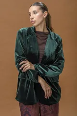 Blazer de terciopelo en color verde profundo, con solapas anchas, cierre frontal con un botón y bolsillos laterales con solapa. Presenta un corte relajado y estructura fluida.