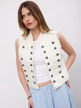 Chaleco vaquero blanco de estilo militar, con doble botonadura frontal de botones oscuros y diseño sin mangas con bordes deshilachados.