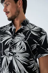 Camisa de manga corta con estampado botánico de hojas en tonos azul y blanco. Presenta cuello clásico, cierre frontal abotonado y corte slim.