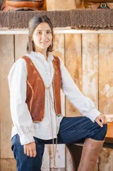 Chaleco artesanal con delantera de cuero marrón y espalda de tejido de punto marrón oscuro. Presenta detalles de bordado en lana alrededor de los bordes y costuras, escote en V y cierre frontal con cordones trenzados.