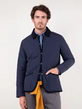 Cazadora acolchada azul marino con cuello de pana negro, cierre con botones a presión y bolsillos laterales.