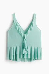 Musculosa de punto color verde menta, con escote en V adornado con volados que caen verticalmente por el centro. El bajo presenta un ruedo con doble capa de volados.