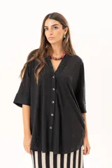 Camisa negra de corte oversize con diseño de encaje calado, escote en V, cierre frontal con botones y mangas tres cuartos. Presenta un diseño asimétrico con la parte posterior ligeramente más larga.