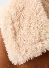 Chaqueta de efecto ante color marrón con forro y cuello de borreguito en tono crema. Presenta cierre frontal con cremallera, diseño recto y dos bolsillos laterales.