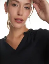 Blusa de satén color verde oscuro, de manga larga abullonada con puños elásticos. Presenta cuello redondo con escote en V y detalles de bordado con mostacillas en el cuello.