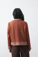 Blazer de gamuza color terracota con bordados decorativos en color crudo en solapas, puños y ruedo. Presenta corte recto, solapas clásicas y cierre frontal con un botón forrado.