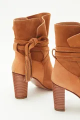 Bota de caña media en gamuzón color suela, con taco cuadrado y tiras envolventes en la caña terminadas en borlas decorativas.