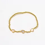 Pulsera elástica de cuentas doradas con tres dijes en forma de corazón con incrustaciones de nácar.