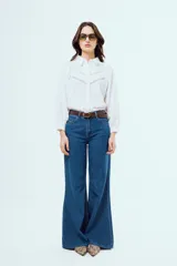 Camisa blanca de manga larga abullonada con puños elásticos, cuello camisero clásico y cierre frontal de botones. Presenta detalles de alforzas y encaje geométrico en la pechera.