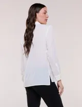 Camisa blanca de corte clásico y caída fluida, con cuello camisero tradicional, abotonadura frontal oculta y mangas largas con puños anchos.