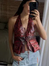 Chaleco top de cuero con efecto desgastado, escote halter profundo y cierre frontal con múltiples tiras para atar. Presenta bolsillos frontales aplicados con detalles de argollas metálicas.