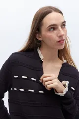 Sweater de punto negro con detalle de calados y lazo en el escote. Tiene ribetes con volados en contraste en el cuello y puños.