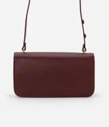 Cartera tipo shoulder bag de tamaño mediano, confeccionada en poliuretano color marrón oscuro. Presenta una solapa frontal con un detalle metálico dorado de forma orgánica y asa ajustable.