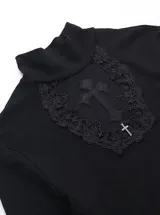 Remera de manga larga negra con cuello alto, confeccionada en viscosa y elastano. Presenta un panel frontal de encaje transparente en el pecho con un aplique de cruz bordada y detalles de cruces en las mangas.