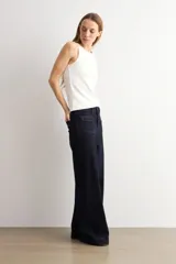 Pantalón de jean azul oscuro con corte flare, tiro alto y bolsillos delanteros tipo plaqué. Presenta costuras a la vista y una silueta amplia en las piernas.