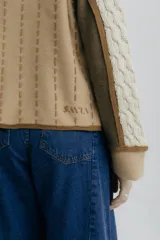 Chaqueta de punto con diseño color block en negro, beige y marrón. Presenta cuello redondo, cierre frontal con botones grandes, bolsillos frontales y detalles de costuras decorativas verticales en color claro.