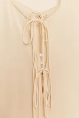 Camisa de viscosa con cuello redondo y escote en pico ajustable mediante lazadas. Presenta cierre frontal con botones, mangas largas con terminación evasé y detalle de volantes en el mismo tejido.