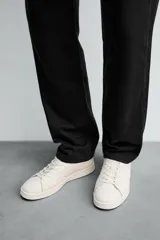 Zapatilla de cordones confeccionada en piel, con horma redonda y suela a tono. Presenta un diseño minimalista con detalle de contraste en el borde del talón.