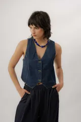 Chaleco de denim azul con cuello en V, cierre frontal con botones metálicos y pespuntes en contraste.