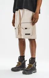 Bermuda color beige de calce relax-fit, con cintura elástica y cordón de ajuste negro. Presenta grandes bolsillos cargo con fuelle en las piernas y un cinturón de cinta negra con hebilla de plástico.