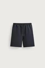 Bermuda tipo jogger de ajuste relajado, color negro, confeccionada en tejido interlock de algodón con elasticidad. Cuenta con cintura elástica ajustable con cordón y bolsillos de vivo en la parte delantera y trasera.