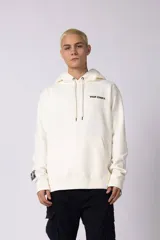Buzo tipo canguro de calce oversize, color off-white, con capucha y cordones ajustables. Presenta un pequeño estampado en el pecho con el texto 'VCP CNPT.' y un parche decorativo en la manga derecha.