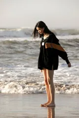 Hoodie negro de tela de toalla, con cuello alto y cierre frontal parcial. Presenta una franja horizontal color mostaza en el pecho y detalles en azul turquesa en el cuello y cordones.