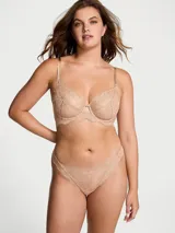 Bombacha tipo tanga de tiro bajo, confeccionada en encaje supersuave color tostado, con detalle de pequeña roseta decorativa en la parte frontal.