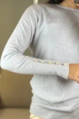 Buzo de hilo negro con cuello redondo, manga larga y detalle de botones decorativos en los puños y a lo largo del antebrazo.
