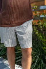 Bermuda a rayas verticales color gris y blanco, de lino imperial, con bolsillos laterales y traseros, y elástico en la cintura.